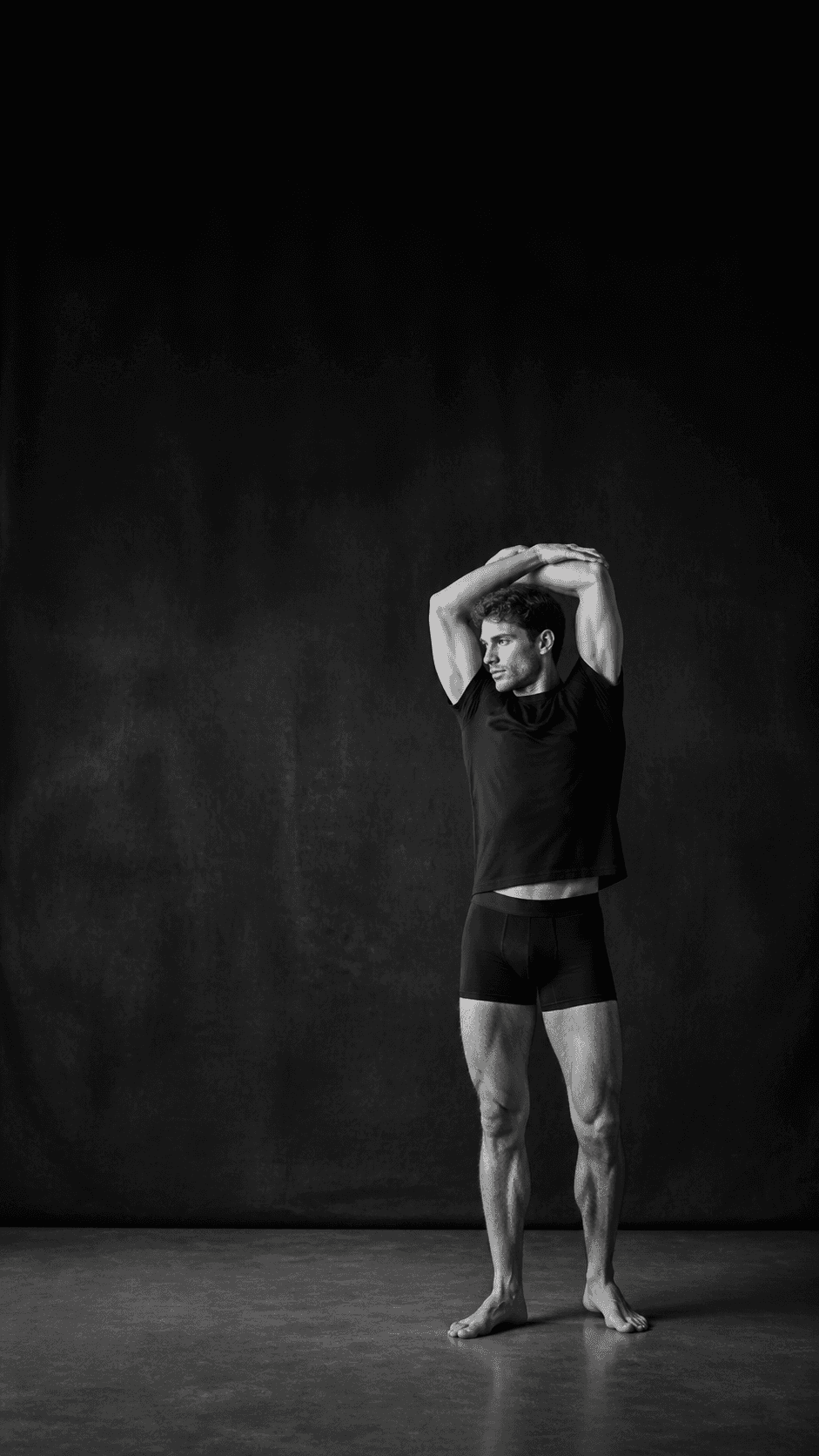 A man stretching in a dark studio while wearing black base layers